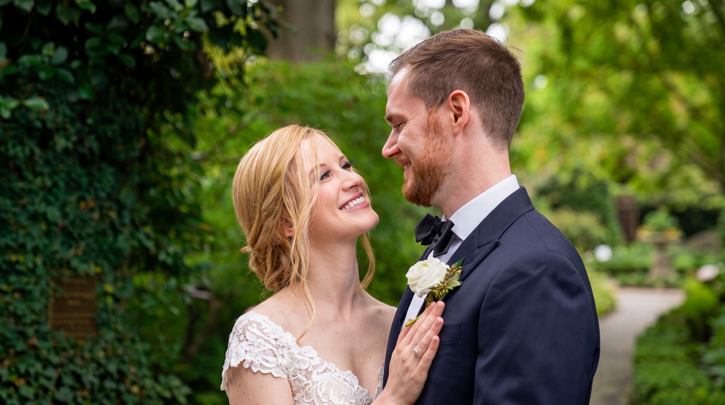 Bride and groom smiling at one another on a garden path