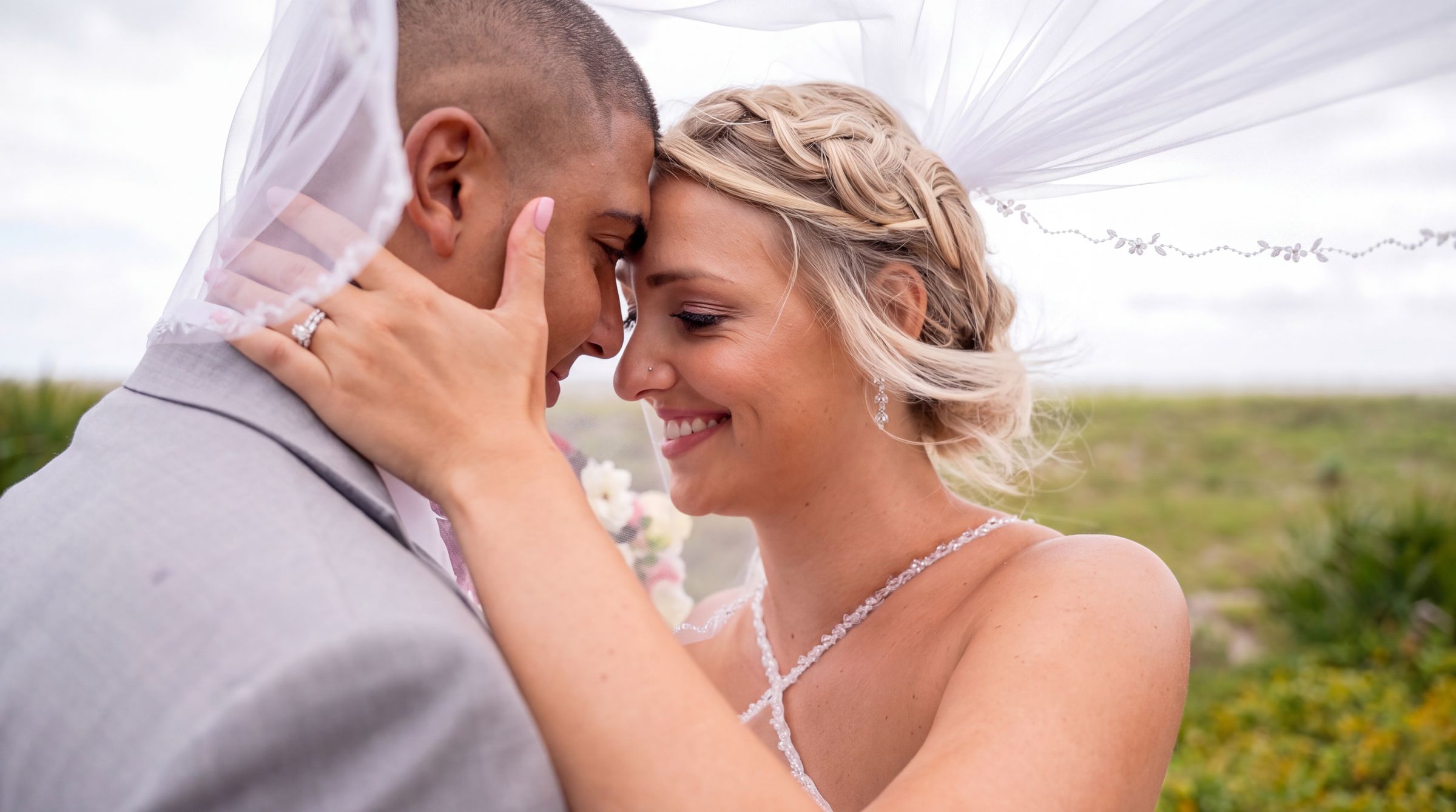 Bride and groom touching foreheads as her veil lifts in the breeze