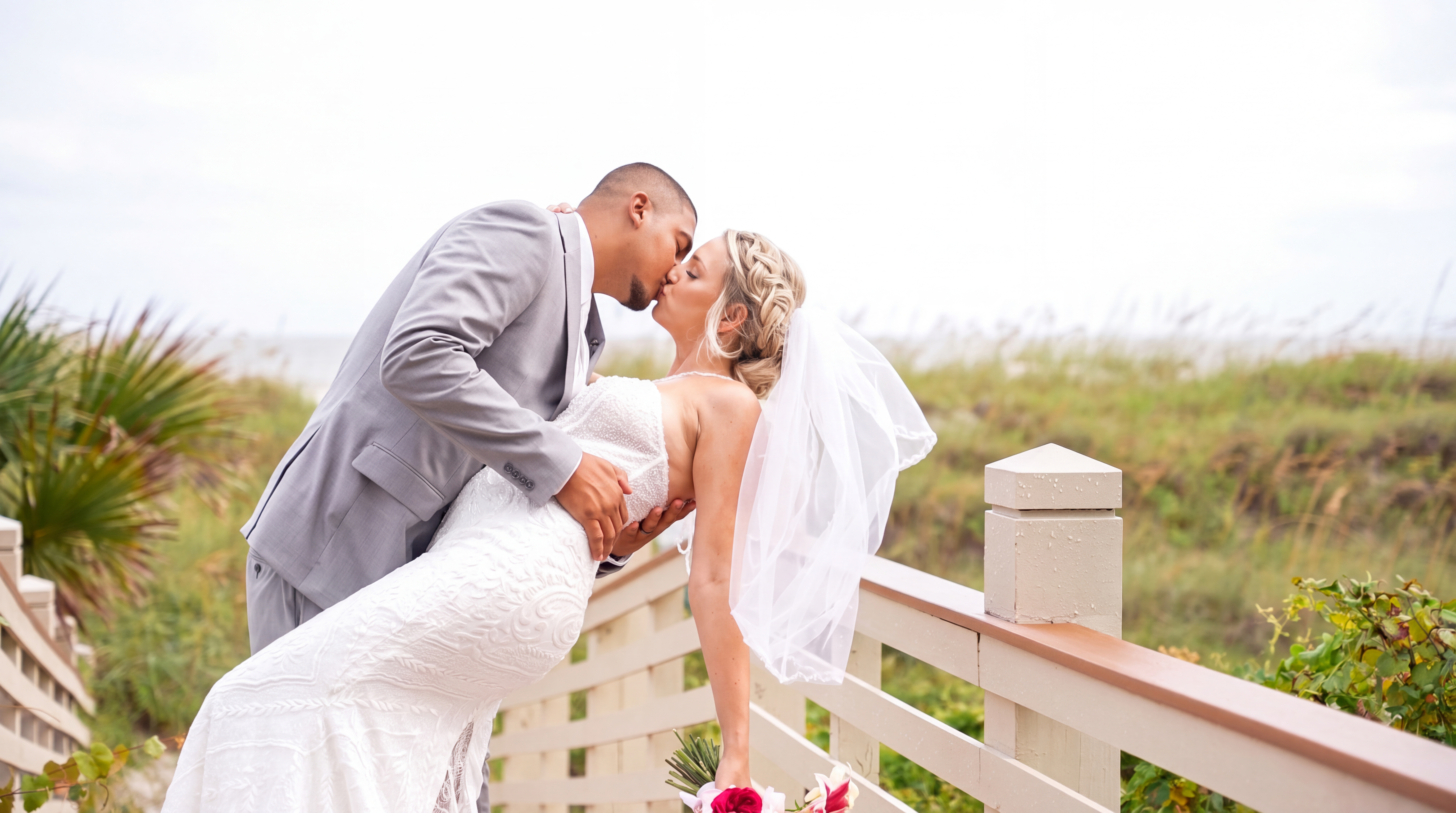 Bride and groom kissing beside a coastal boardwalk after their wedding