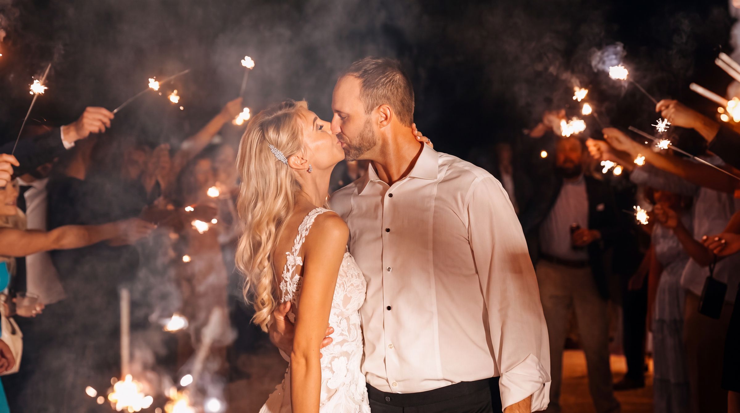 Newlyweds kissing as guests hold sparklers during their wedding send-off
