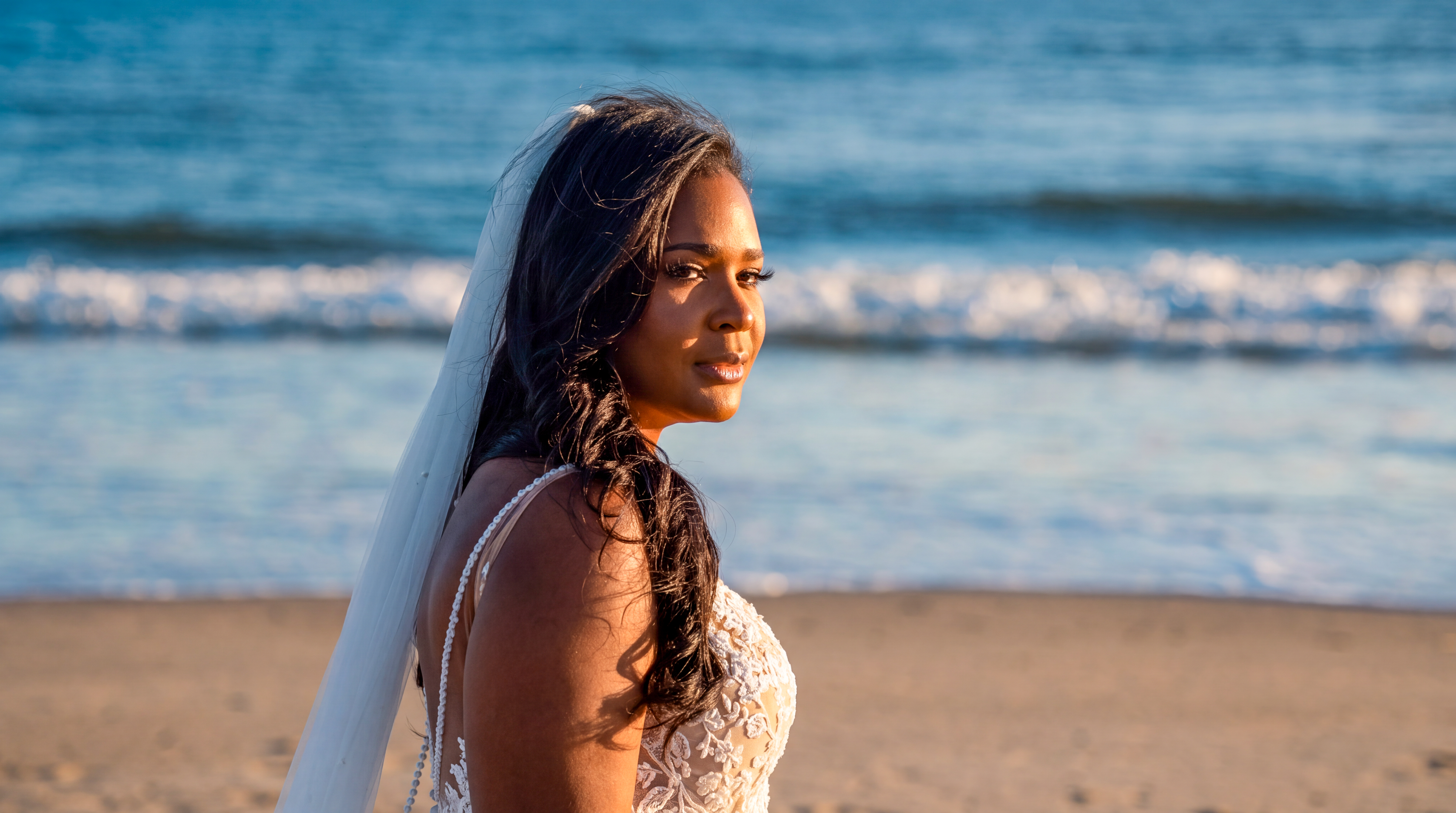 Bride in her wedding dress standing on the beach at sunset