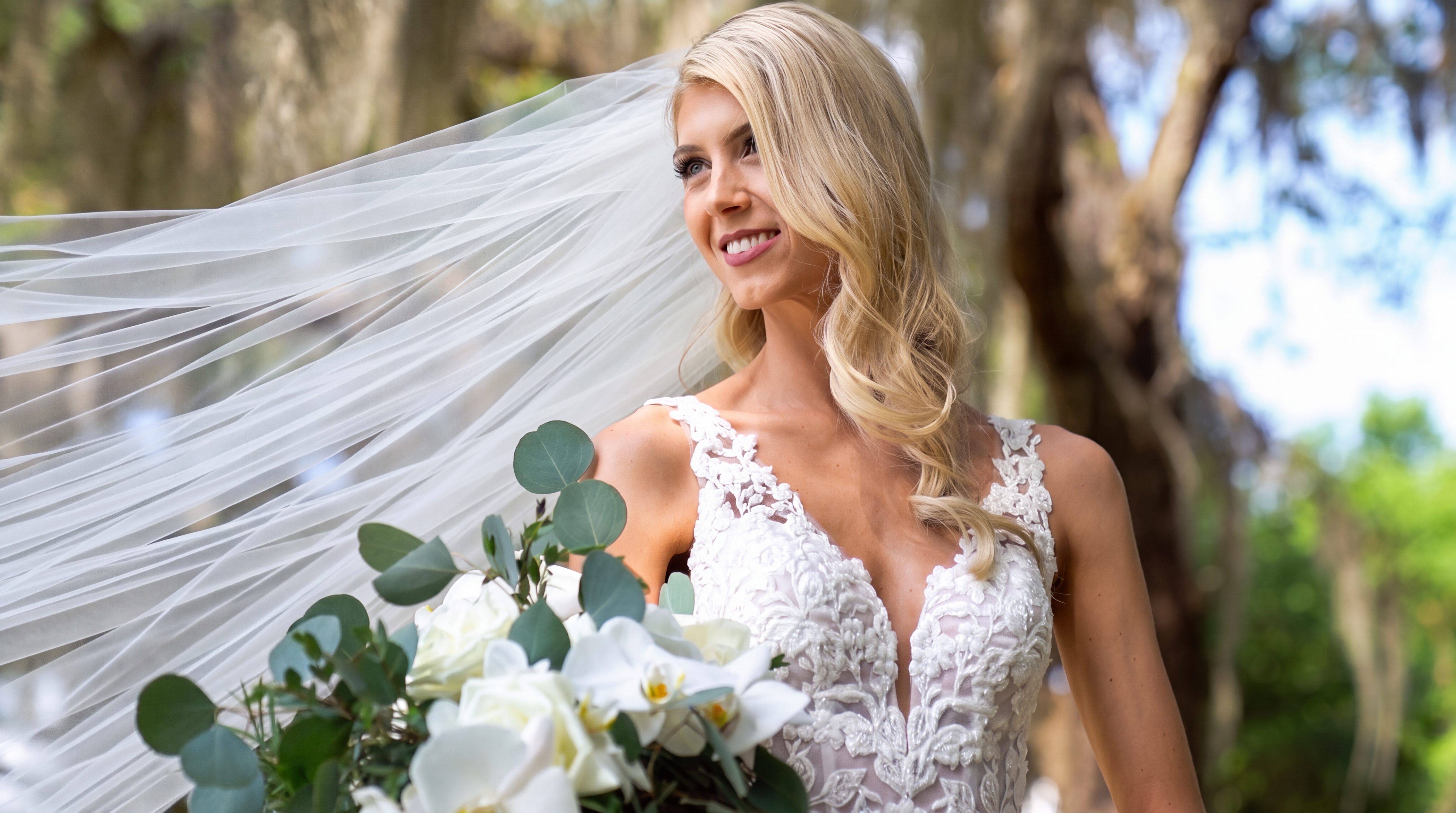 Bride holding a white-and-green bouquet with her veil flowing behind her